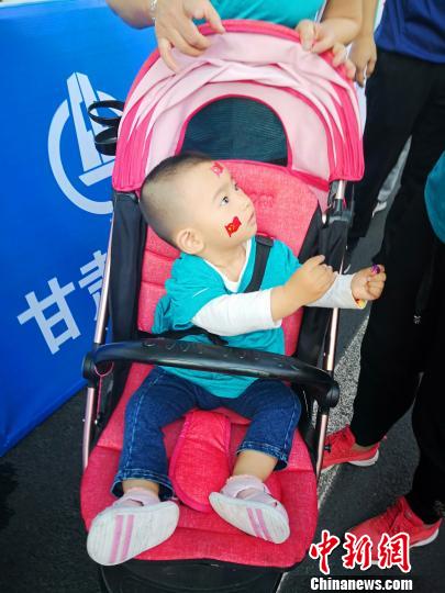 图为小宝宝身穿幼儿定制版运动服，在童车里摇旗呐喊。　史静静　摄