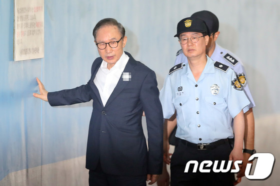20日,李明博用手扶墙走进法院